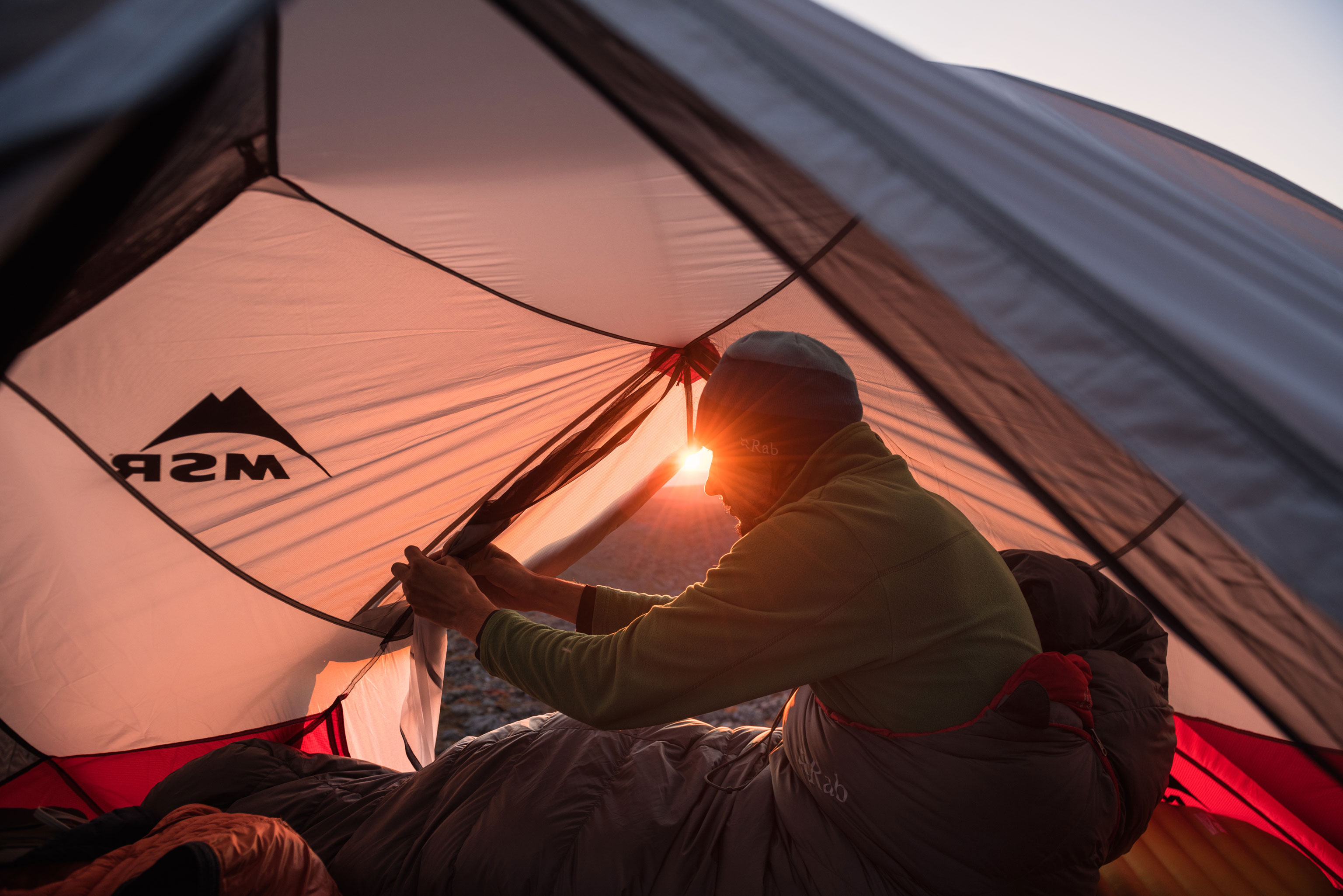 Wanderer öffnet das Zelt bei Sonnenaufgang