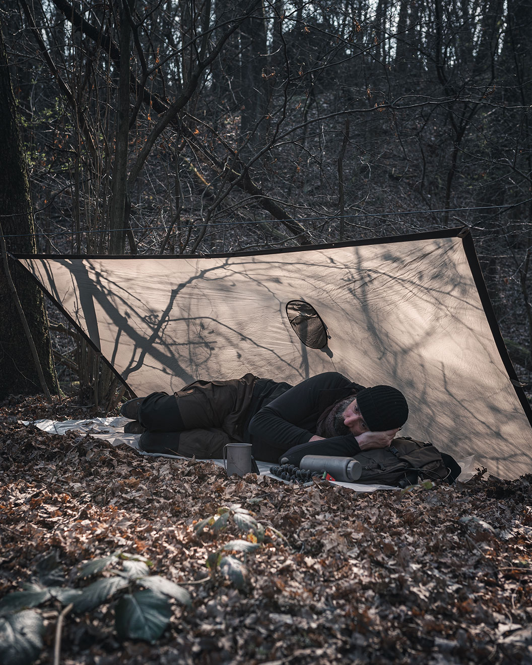 How to bushcraft: Bushcraft survival expert Alex Wander lying underneath a tarpaulin in the forest