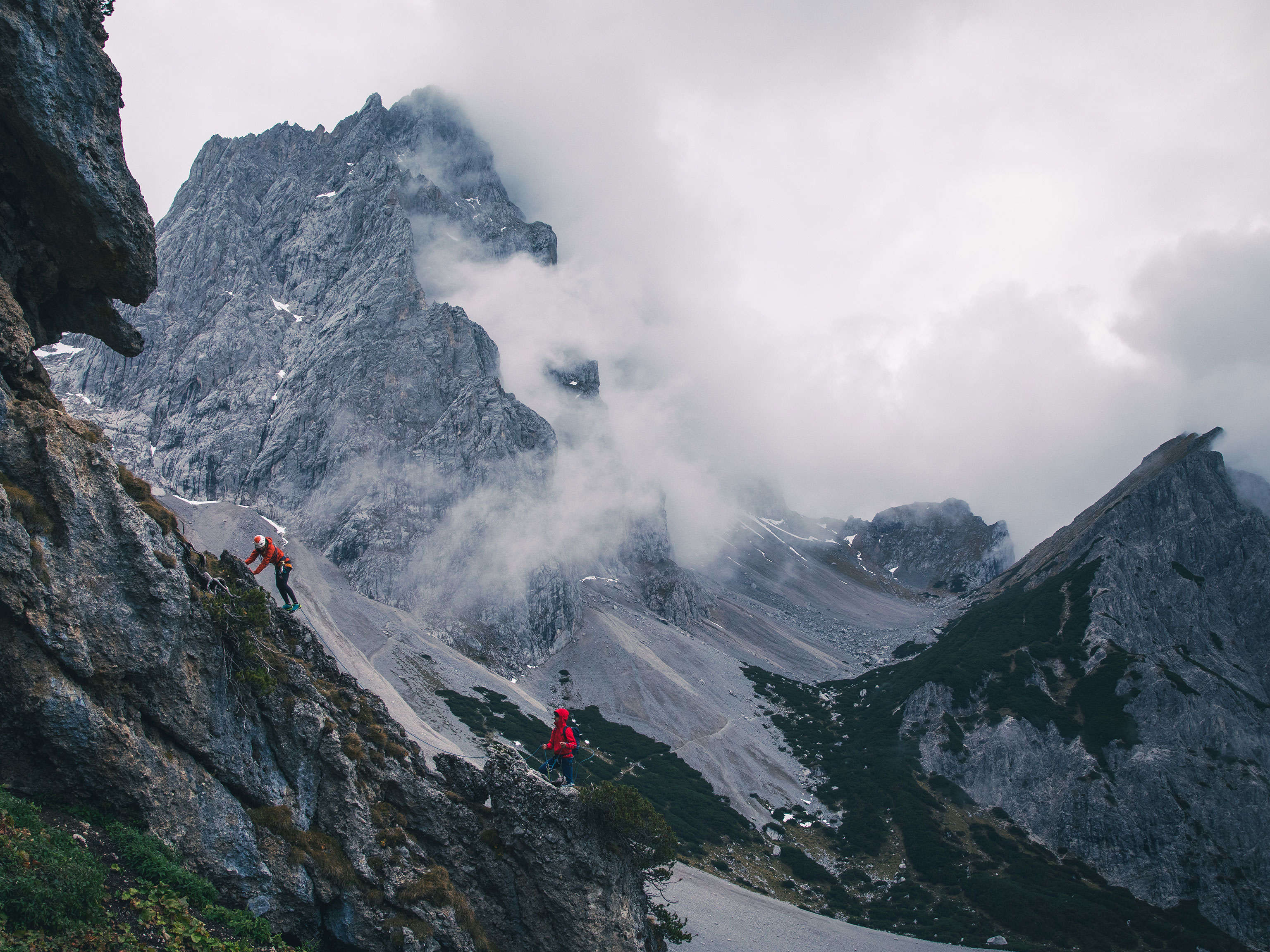 Zwei Bergsteiger klettern an einem Grat vor dem Hintergrund hoher Berge