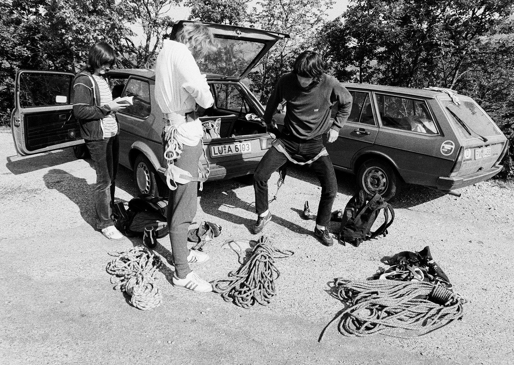 Three climbers putting on their harnesses by parked cars