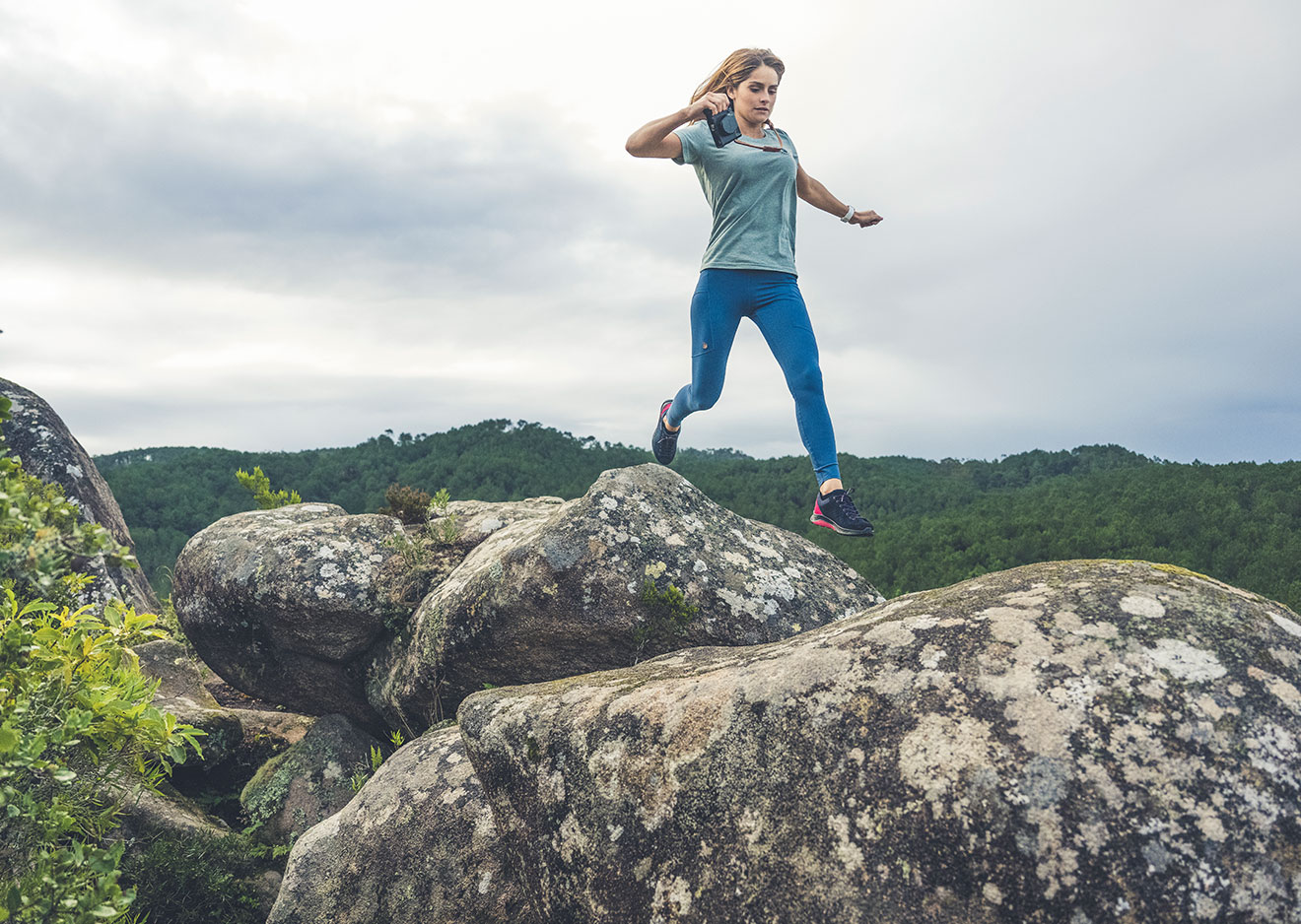 Eine Frau springt über Felsen vor den bewaldeten Hügeln von Sintra