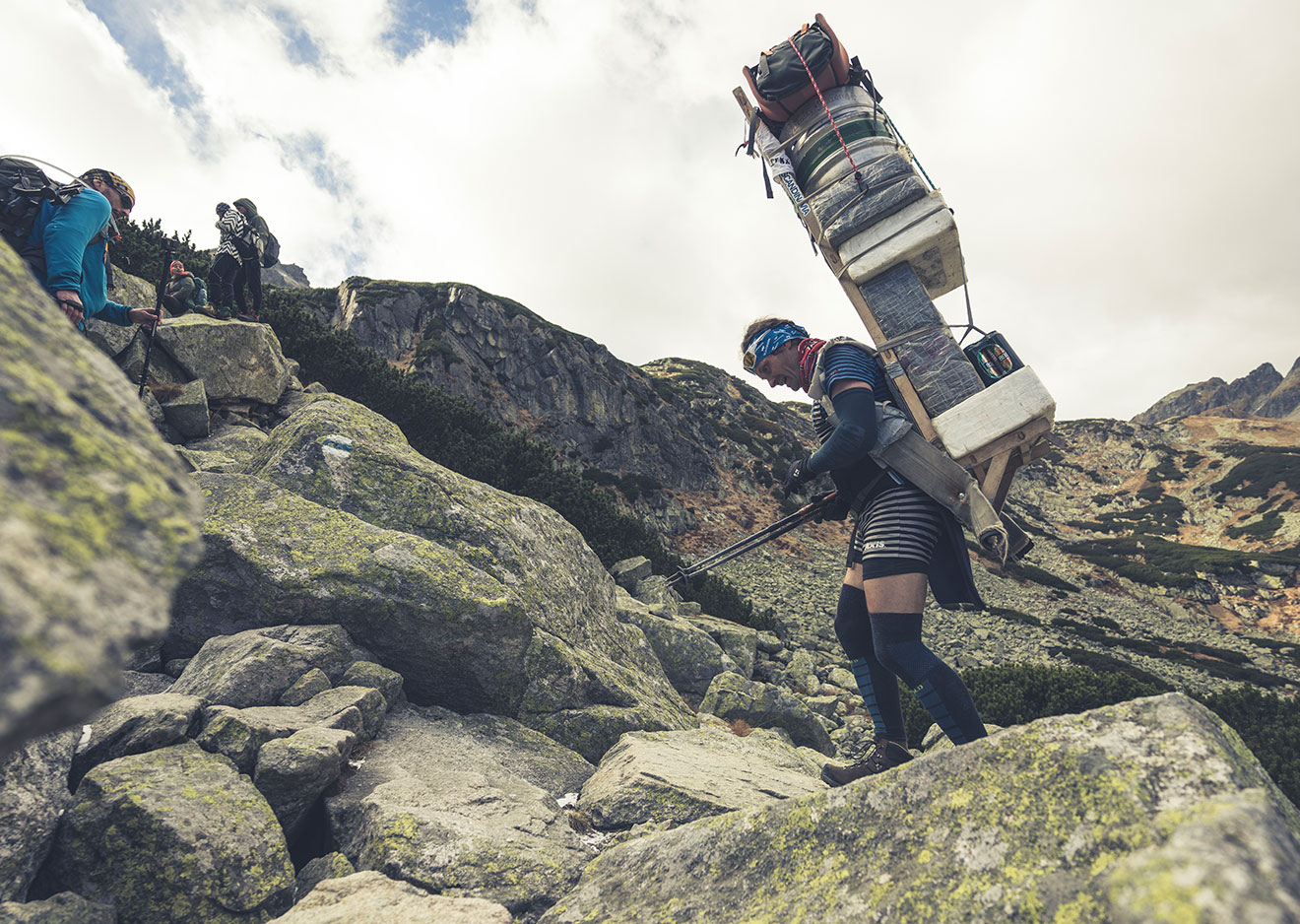 Ein Tatra Sherpa trägt seine voll beladene Kraxe über einen Hang voller großer Felsen