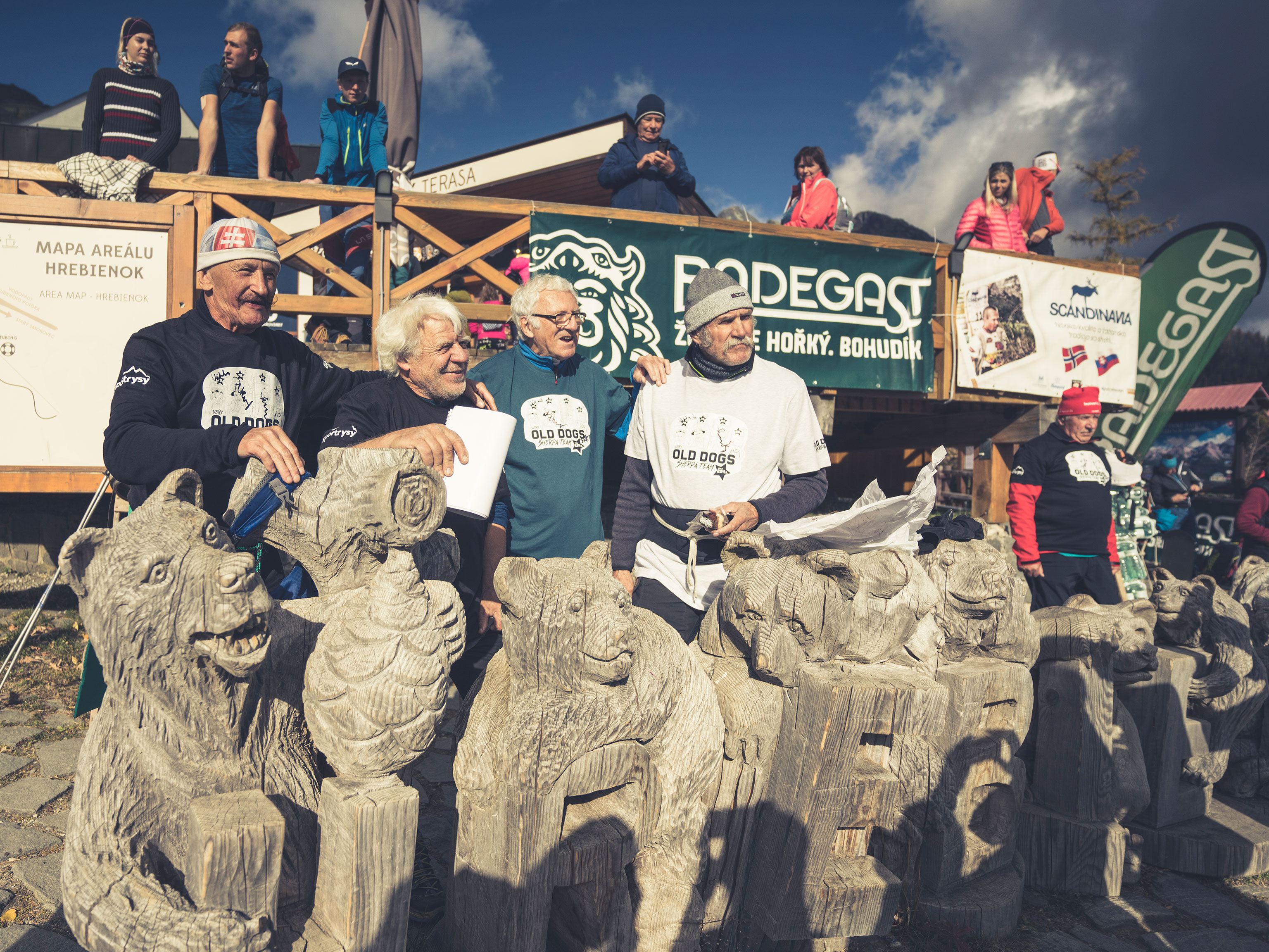 Vier Organisatoren der Tatra Sherpa Rallye posieren hinter Holzfiguren