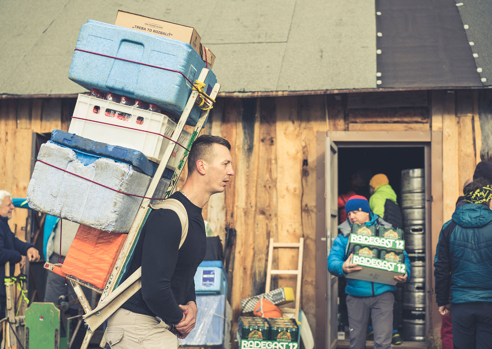 Vor einer Holzhütte, die als Warenlager dient, beladen die Tatra Sherpas ihre Kraxen mit Kisten und Fässern