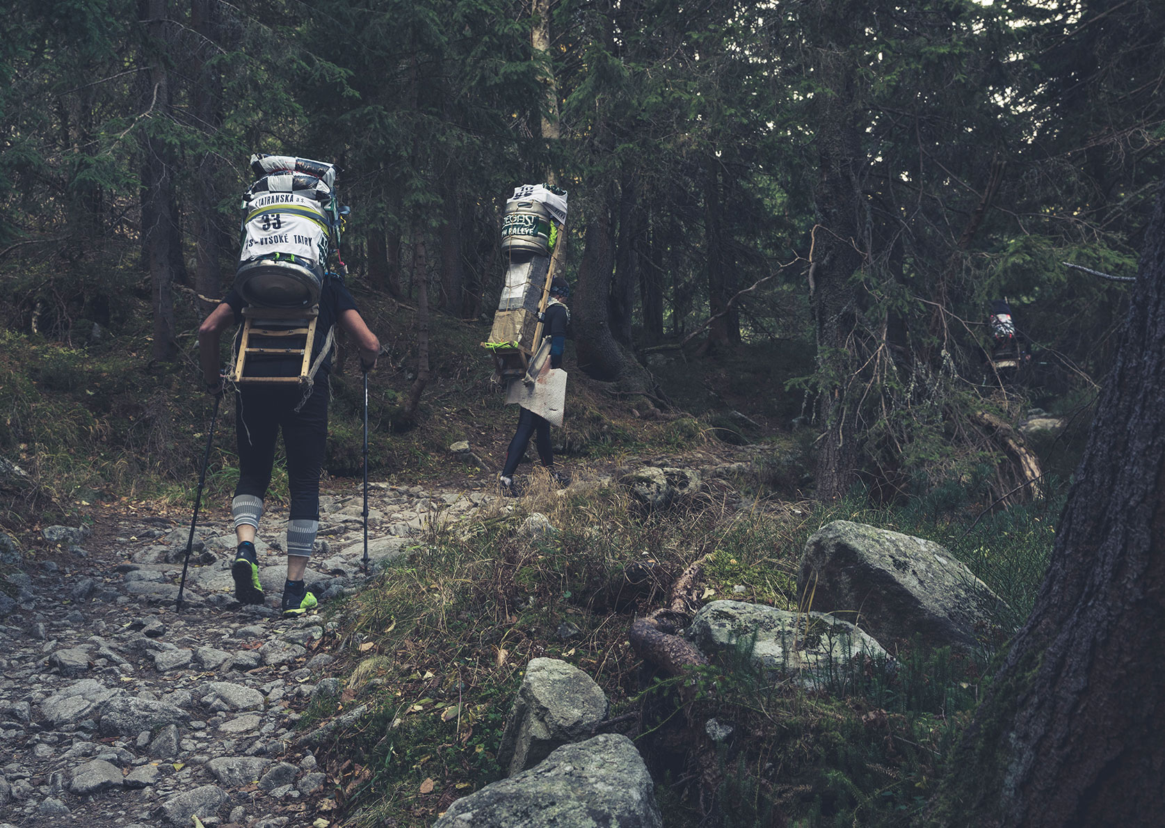 Zwei Teilnehmer der Tatra Sherpa Rallye tragen ihre beladenen Kraxen durch einen Wald