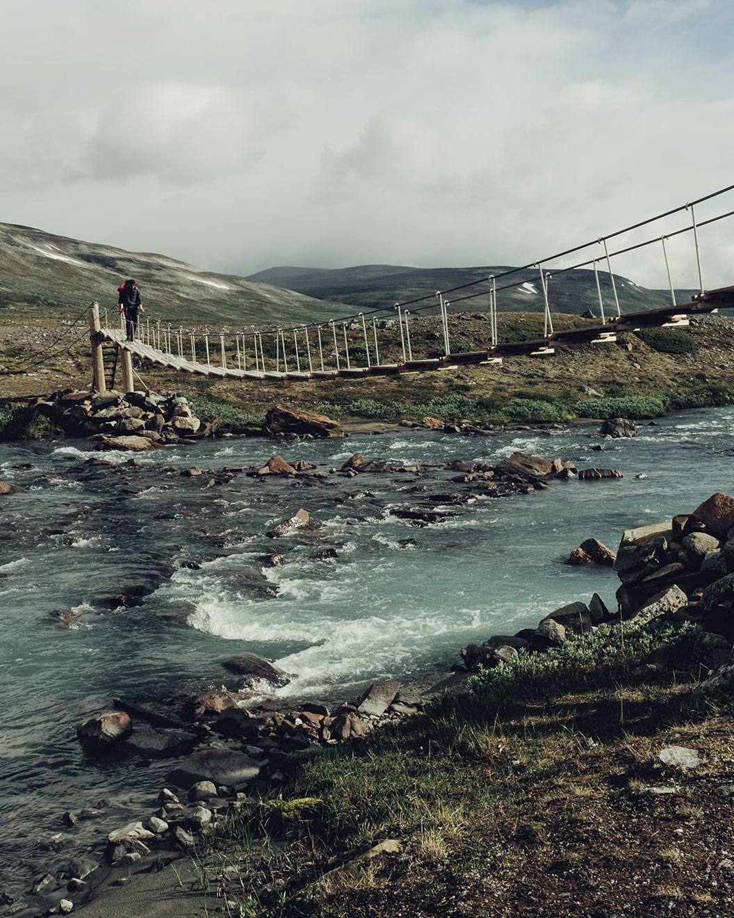Ein Wanderer überquert beim Jotunheimen Trekking einen Fluss über eine Hängebrücke