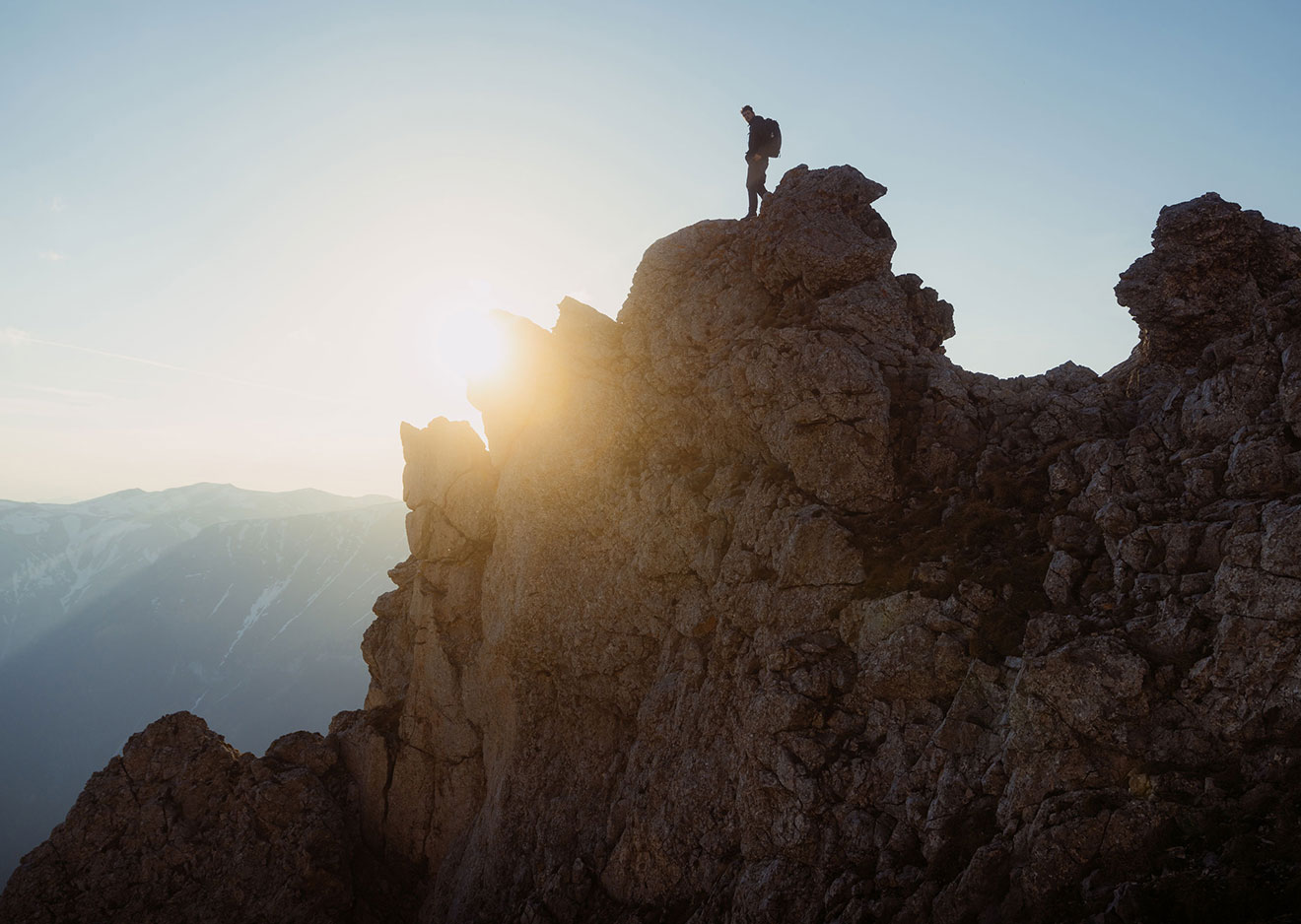 Ein Bergsteiger auf einem exponierten Gipfel vor der aufgehenden Sonne