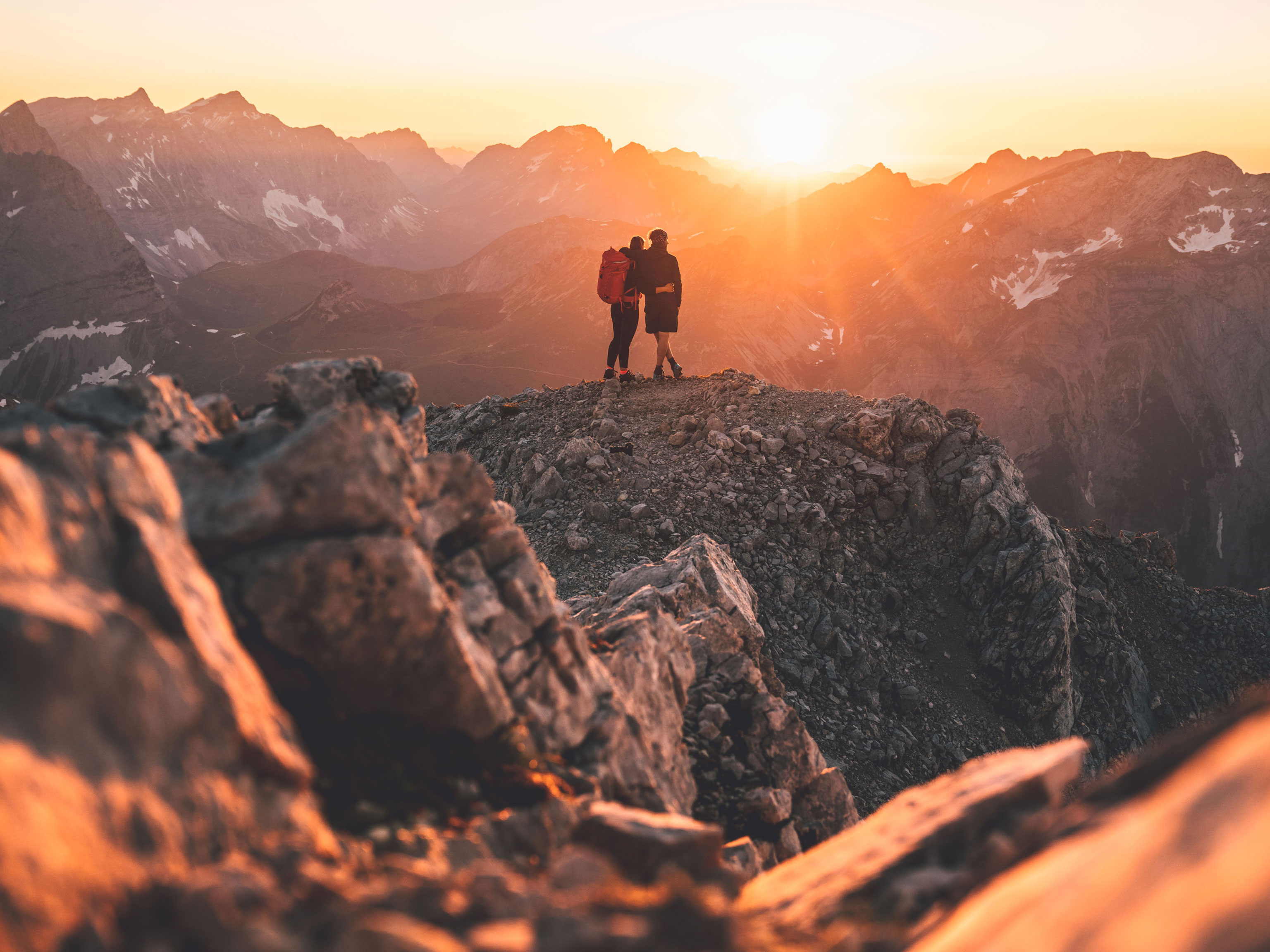 Zwei Bergsteiger betrachten den Sonnenuntergang von einem Felsen aus