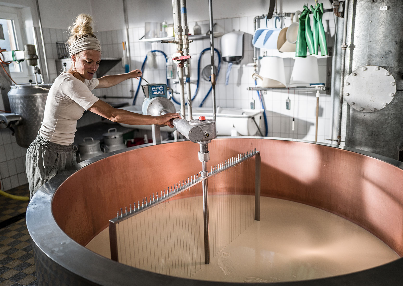 Katharina uses a cutting instrument to stir milk in a copper vat